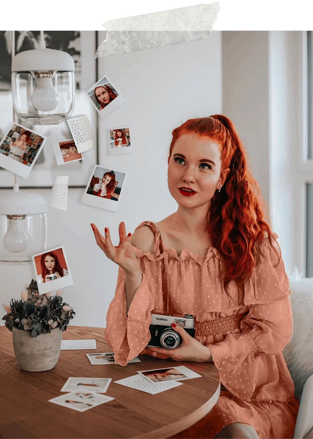Fee sitzt am Tisch, hält eine Sofortbildkamera und lacht, vor ihr liegen Polaroids