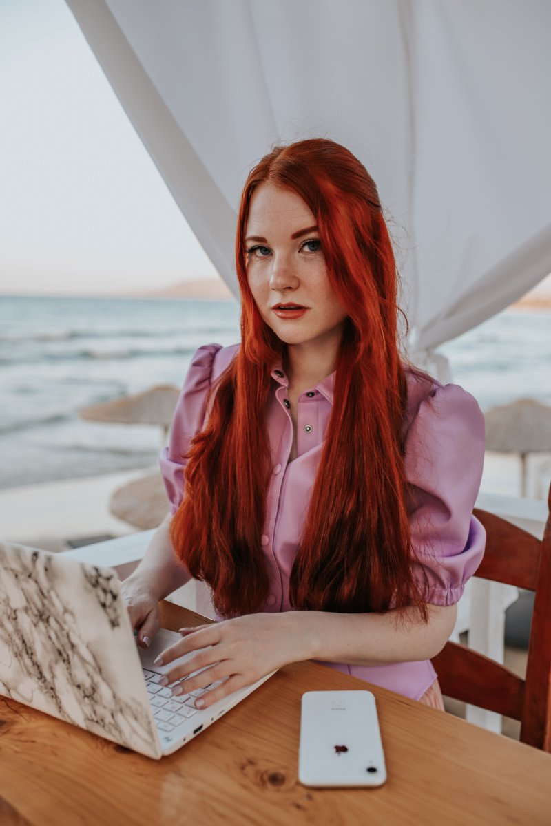 Fee sitzt mit rotem Haar am Laptop an einem Tisch am Meer