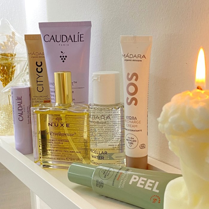 Beauty-Produkte von Caudalie, Nuxe und Mádara vor einer brennenden Kerze auf einem Regal